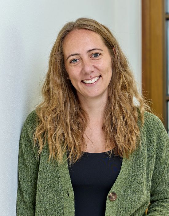 Frau mit langen blonden Haaren gruene Strickjacke lacht entspannt beim Posieren