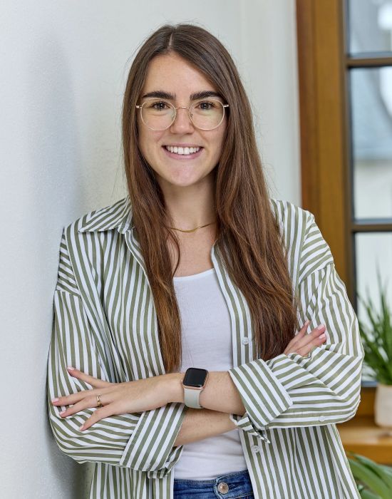 Junge Frau mit Brille gestreiftes Hemd und Smartwatch laechelt in die Kamera