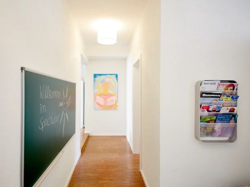 Heller Flur mit Tafel und Zeitschriftenhalter und Kunstbild am Ende des Gangs